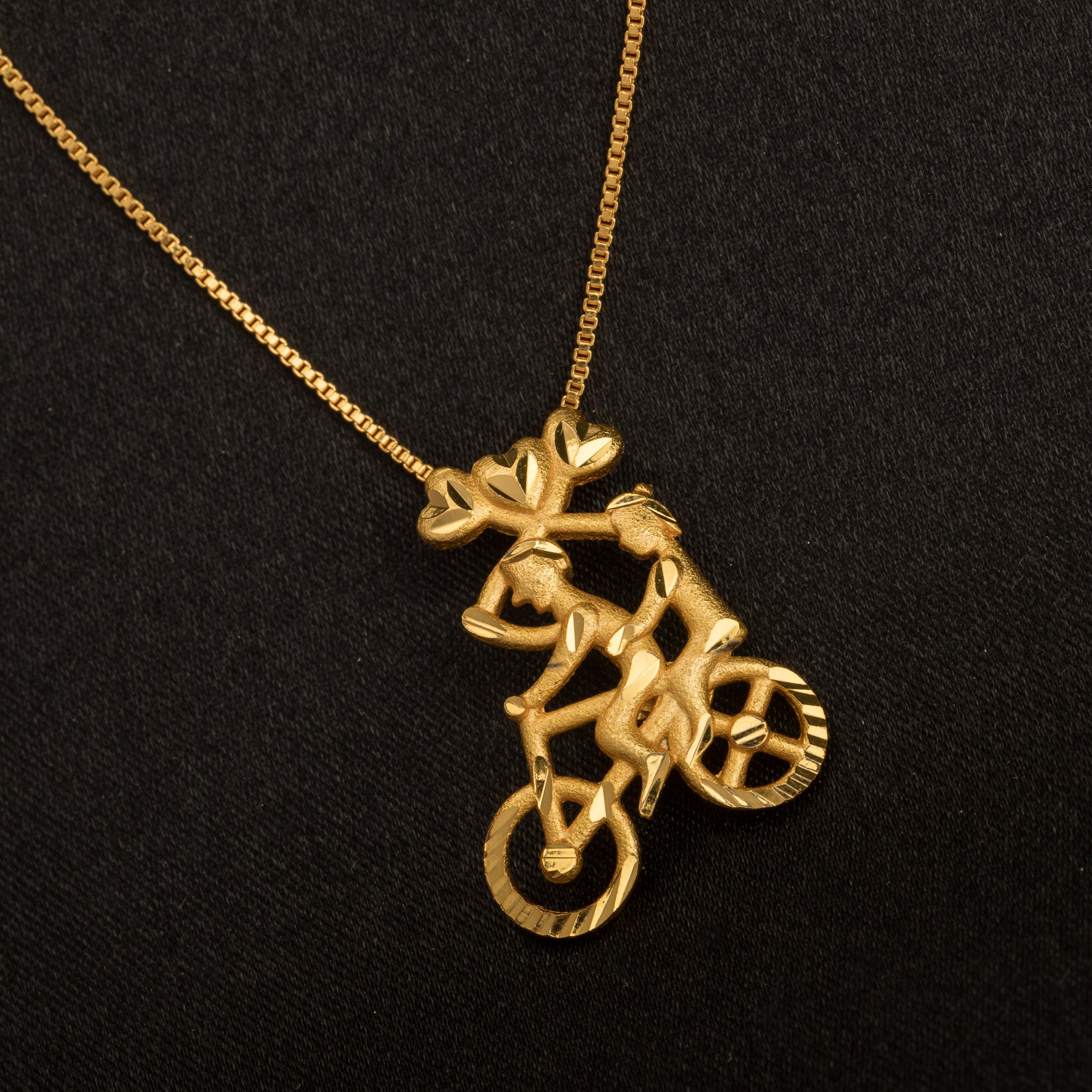 "Gold-tone pendant featuring a boy riding a bicycle, perfect for casual wear, with a fun and unique design."
