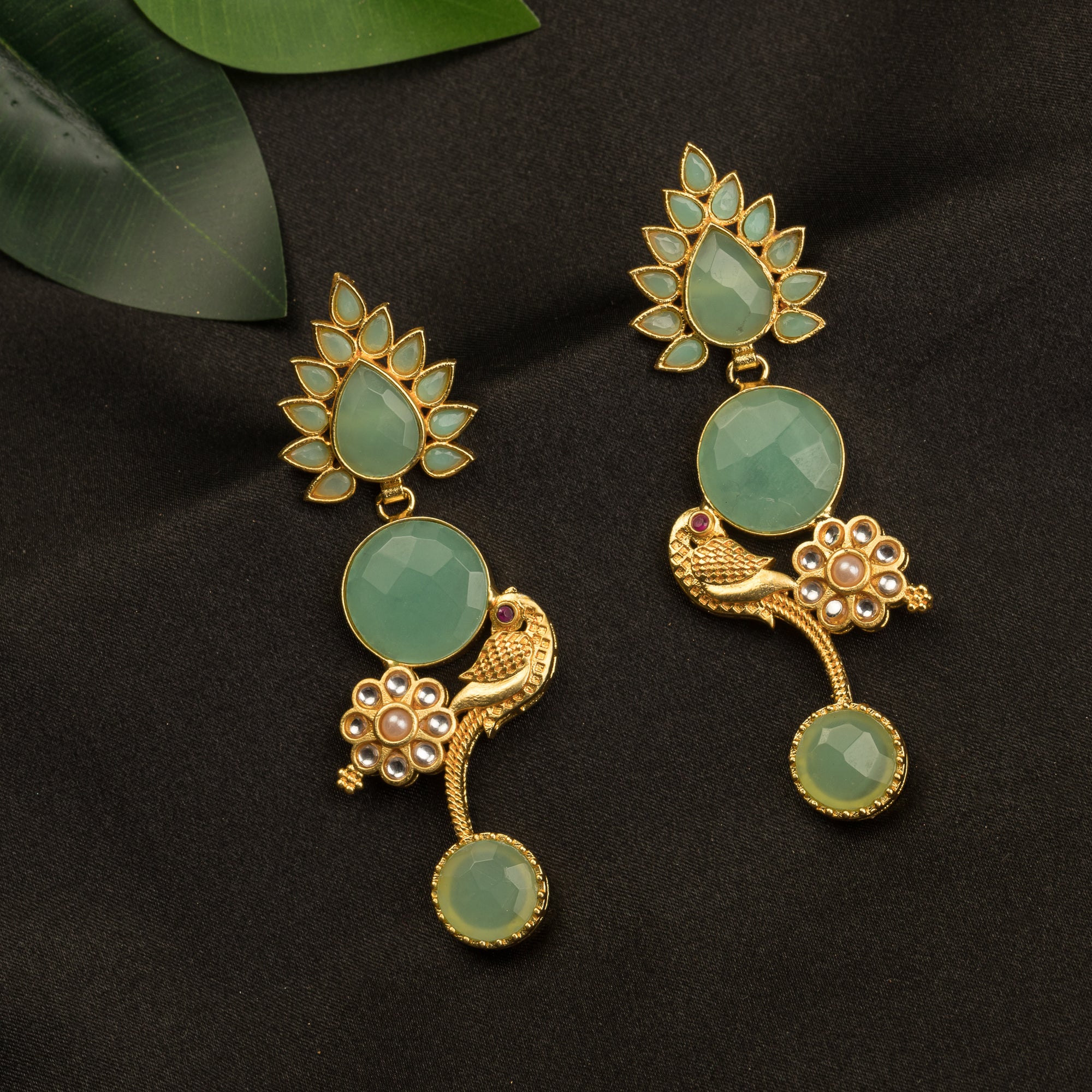 "Gold-tone dangler earrings with light green accents blend warmth and freshness for a chic, eye-catching festival look."
