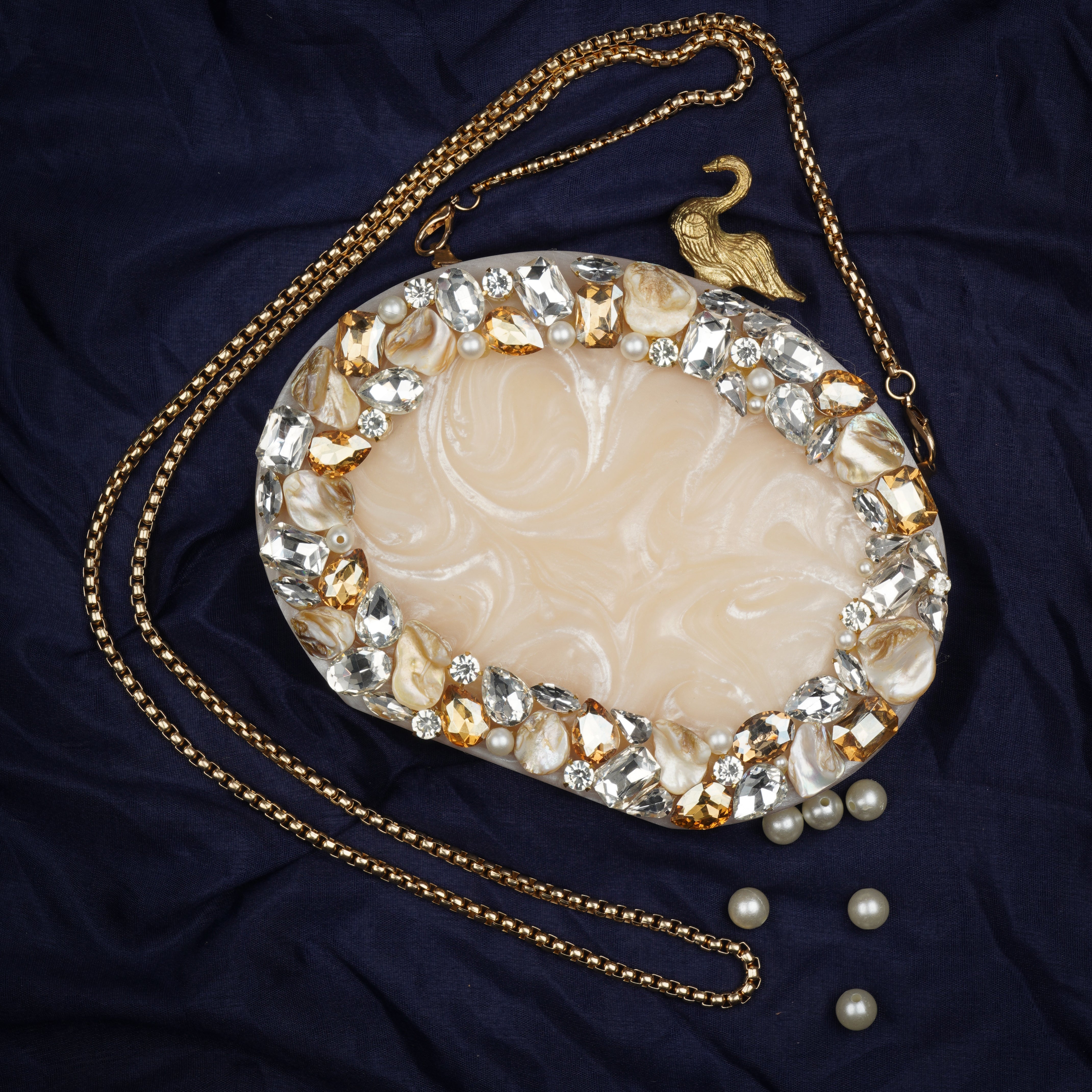Oval-shaped salmon resin clutch with peacock design closure and sleek sling chain for style.
